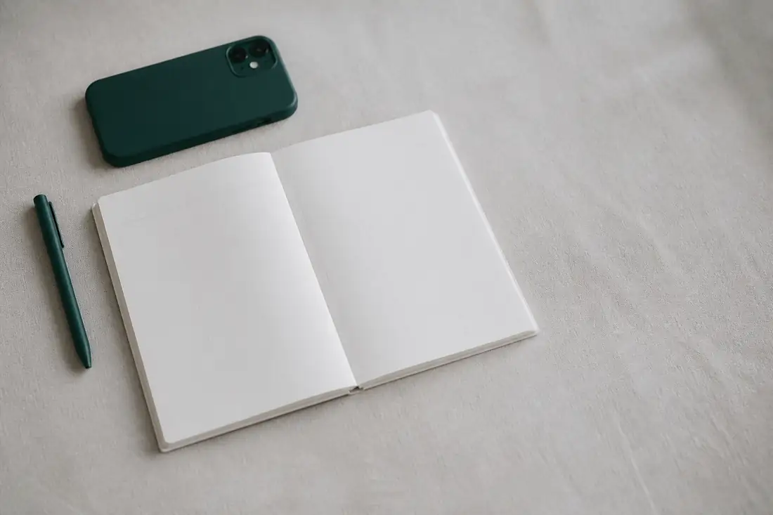 An open weekly planner with every day column blank, a phone lying face down beside it.